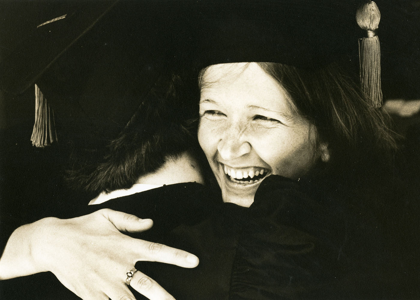 A graduate embracing another person and smiling at the 1984 Commencement Ceremony