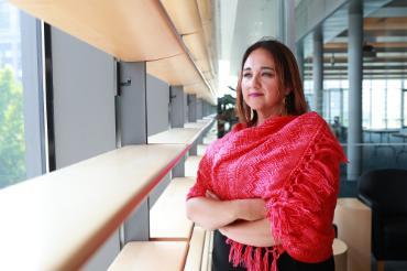 Fe LopezGaetke '06 stands and looks out a window with a pink shawl wrapped around her shoulders.