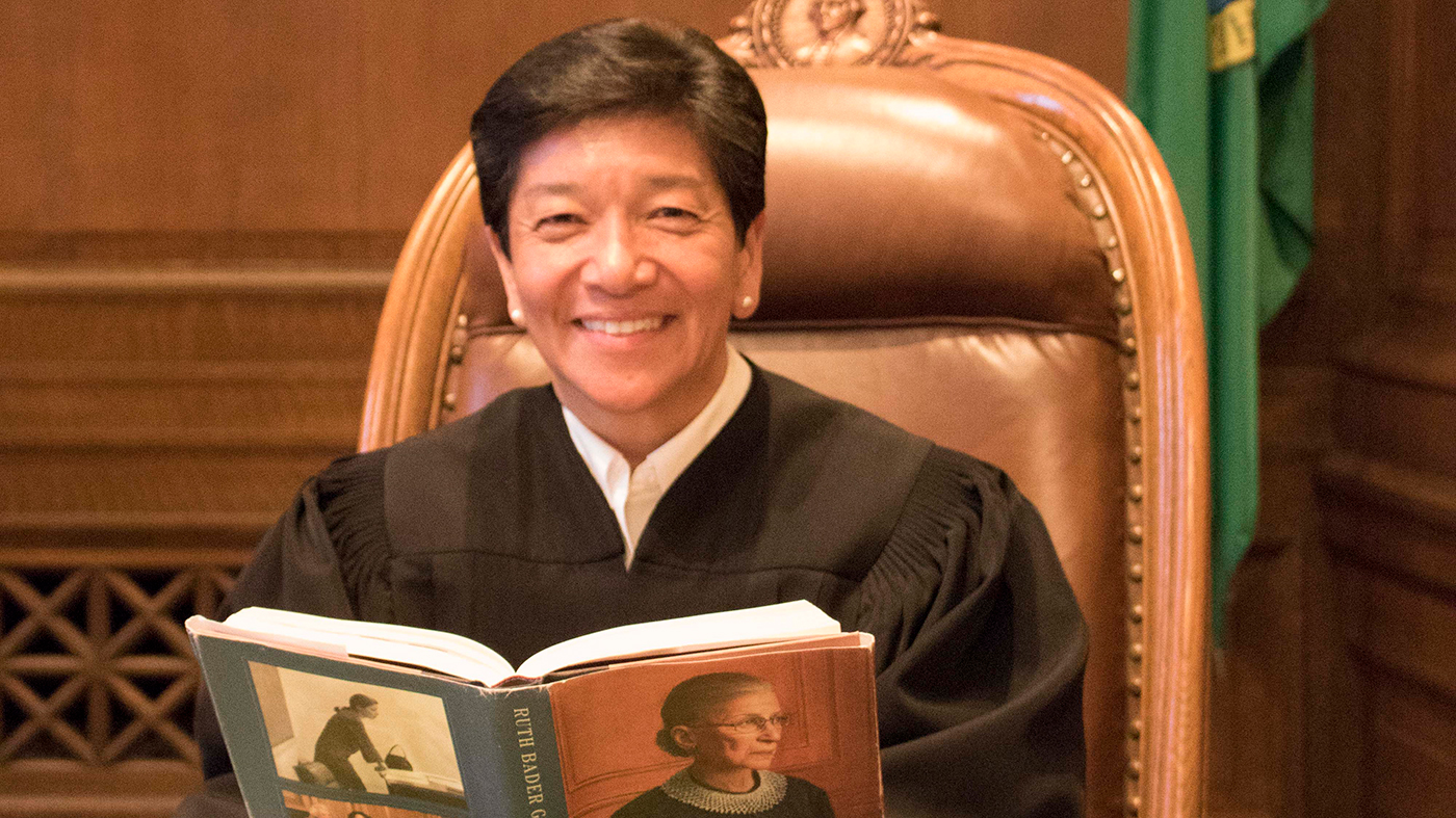 Retired Washington Supreme Court Justice Mary Yu holding a book with the late U.S. Supreme Court Ruth Bader Ginsburg on the cover